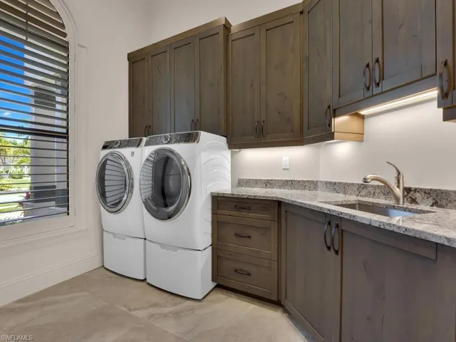 Laundry area featuring a large arched window with blinds, under-cabinet lighting, a built-in sink, wood-finish cabinetry, and stone-finish countertops