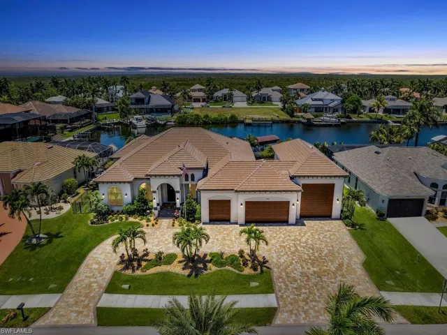 Expansive waterfront residence featuring a barrel tile roof, paver driveway, three-car garage, and established landscaping