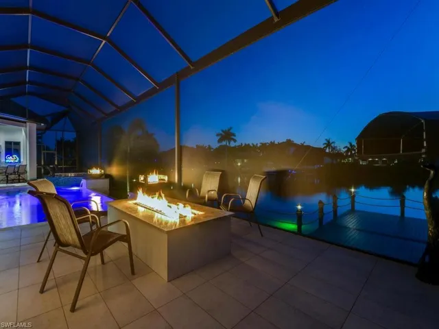 Screened lanai featuring a fire pit, water feature with blue lighting, tiled patio, and a dock on the water