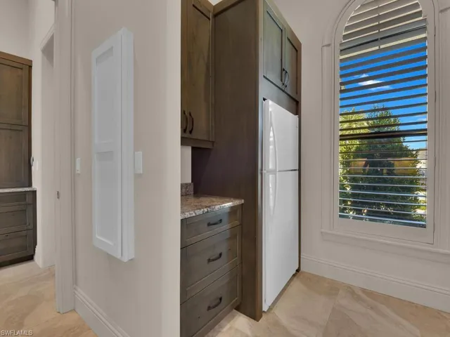 Arched window with plantation shutters, dark wood-finish cabinetry, stone countertop, integrated refrigerator, and wood-finish flooring