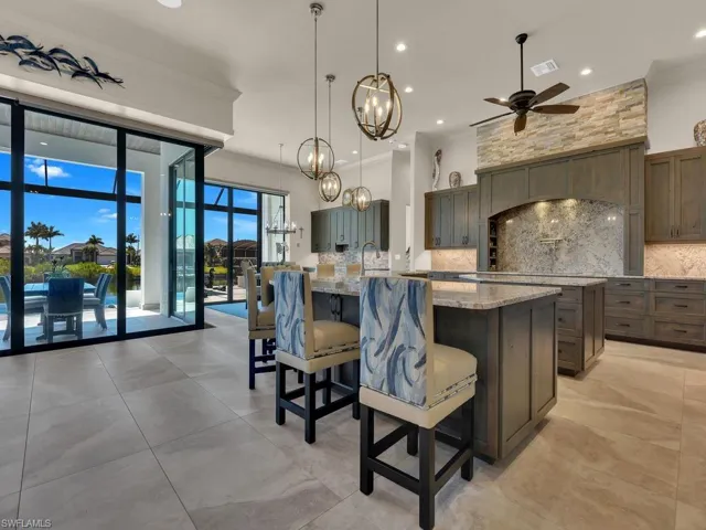 Spacious kitchen featuring an expansive center island with seating, pendant lighting, stone countertops, custom cabinetry, and large format tile flooring