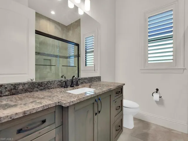Bathroom vanity with a light-toned stone countertop, integrated sink, and dark bronze-finish fixtures