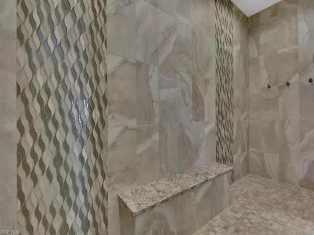 Spacious walk-in shower featuring large format wall tiles, a granite-topped bench, and decorative wave-patterned accent tiles