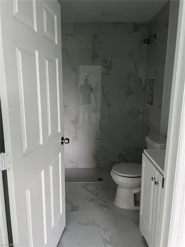 Bathroom featuring a tile shower, tile flooring, toilet, and vanity
