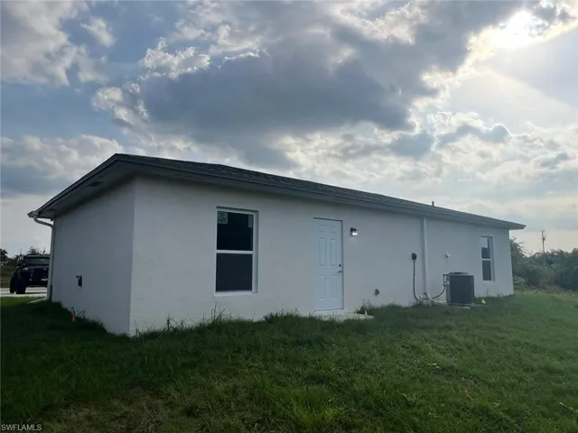 Back of house with a yard and central AC unit