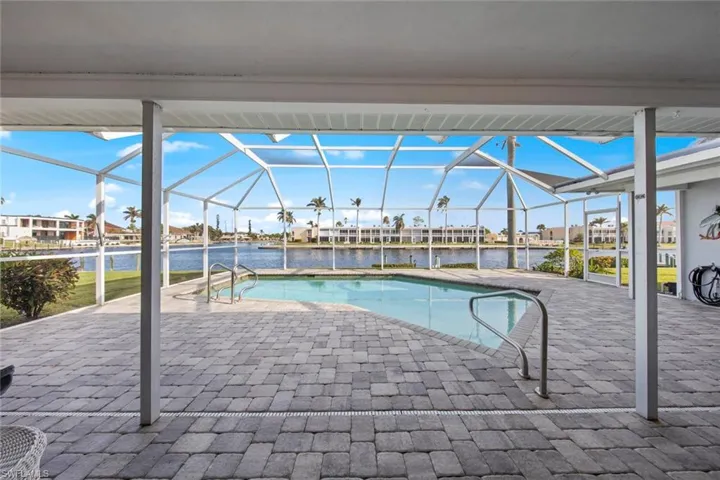 View of swimming pool with glass enclosure, a patio area, and a water view