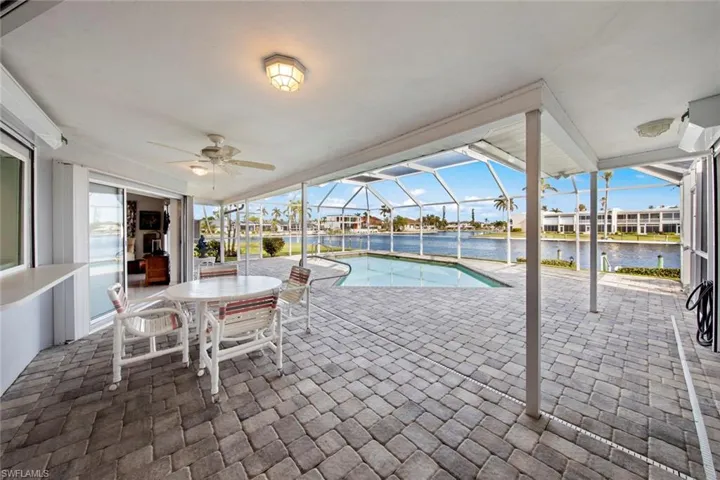 View of swimming pool featuring a patio, a water view, glass enclosure, and ceiling fan
