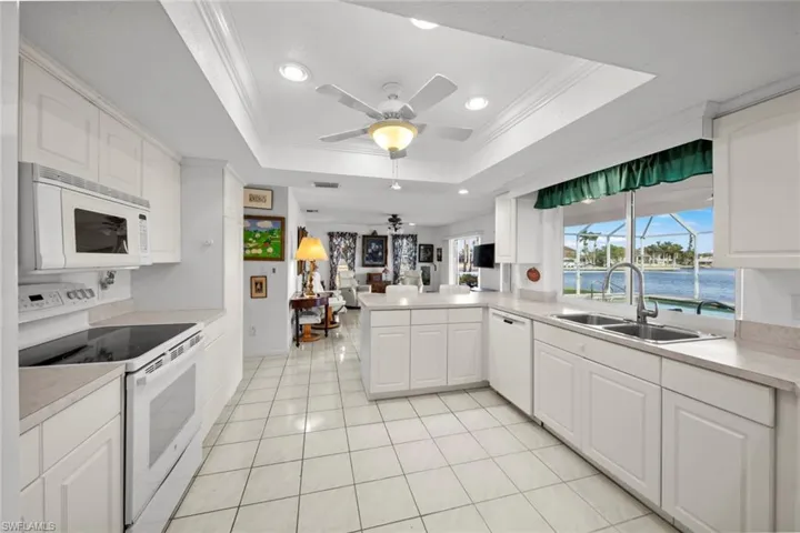 Kitchen with white cabinets, white appliances, kitchen peninsula, and a tray ceiling