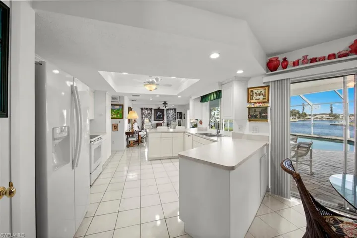 Kitchen with kitchen peninsula, white appliances, a tray ceiling, a water view, and white cabinetry