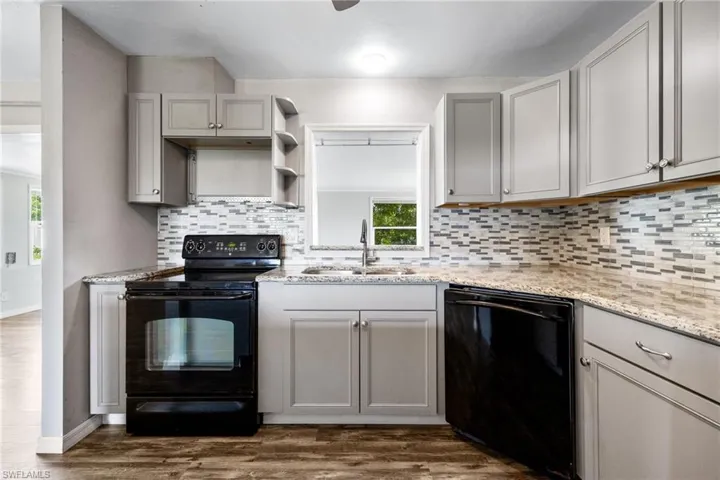 Kitchen with gray cabinetry, black appliances, dark wood-style floors, and backsplash