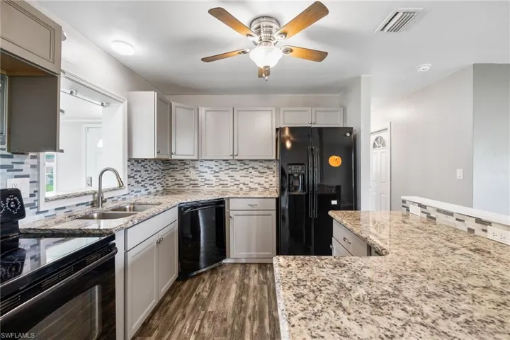 Kitchen featuring black appliances, decorative backsplash, light stone countertops, and a ceiling fan