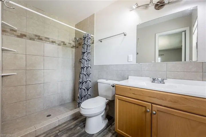 Bathroom featuring vanity, a stall shower, tile walls, and dark wood-style floors