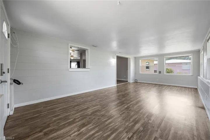 Empty room with concrete block wall, dark wood-style floors, and a ceiling fan