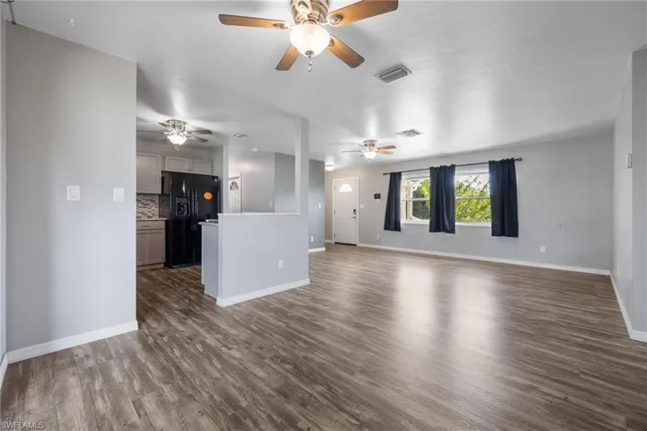 Unfurnished living room featuring dark wood-style floors and baseboards