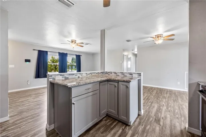 Kitchen with gray cabinets, dark wood-type flooring, a kitchen island, light stone countertops, and decorative backsplash