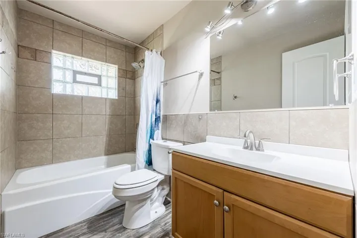 Full bathroom featuring shower / bathtub combination with curtain, tile walls, vanity, and dark wood-type flooring