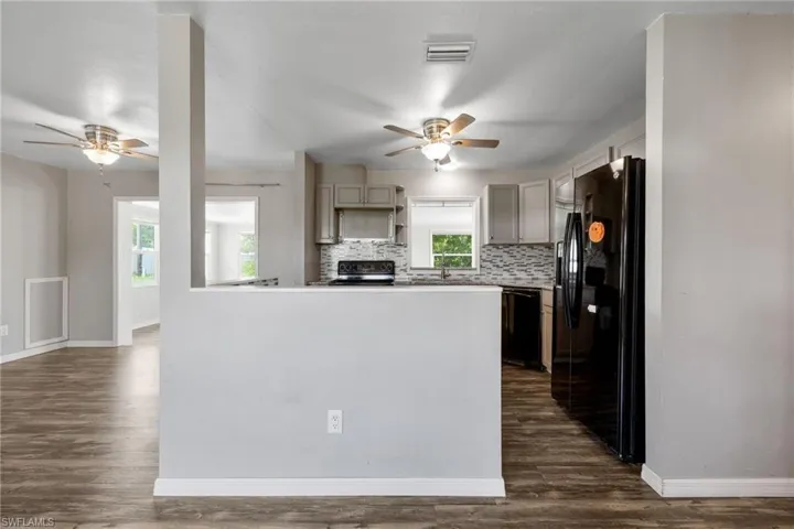 Kitchen featuring ceiling fan, black appliances, tasteful backsplash, and dark wood-style flooring