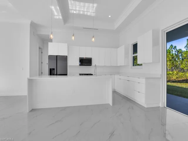 Kitchen featuring appliances with stainless steel finishes, a tray ceiling, decorative light fixtures, and white custom wood cabinetry