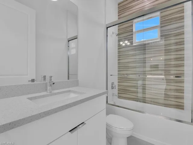 Full bathroom featuring toilet, vanity, and combined bath / shower with glass door.