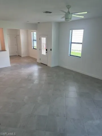 Tiled spare room featuring a ceiling fan and baseboards