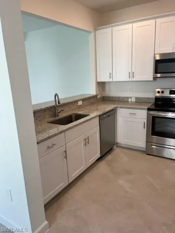 Kitchen with stove, dishwashing machine, a sink, white cabinets, and light stone counters