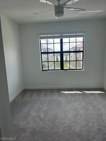 Spare room featuring a ceiling fan, healthy amount of natural light, dark carpet, and baseboards