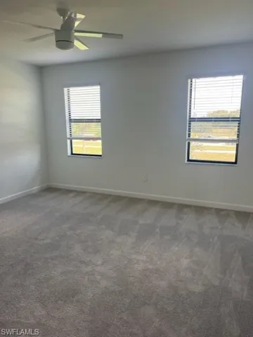 Unfurnished room featuring healthy amount of natural light, dark carpet, and baseboards