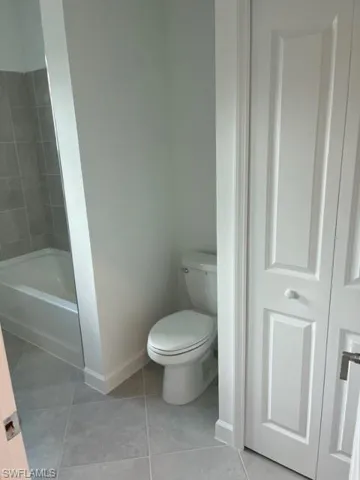 Bathroom with baseboards, toilet, tile patterned floors, and tub / shower combination