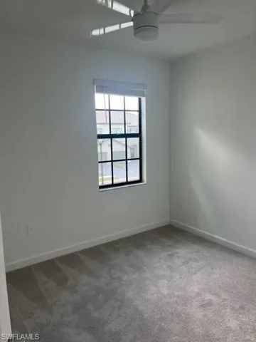 Carpeted empty room featuring a ceiling fan and baseboards