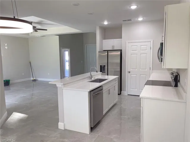 Kitchen featuring hanging light fixtures, appliances with stainless steel finishes, white cabinets, and an island with sink