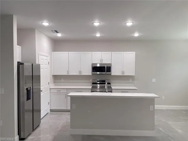 Kitchen with white cabinetry, light tile patterned floors, an island with sink, and stainless steel appliances