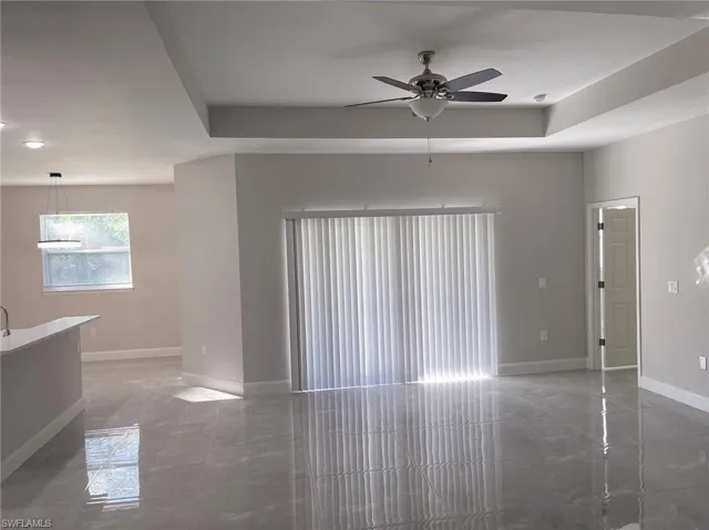 Tiled empty room with ceiling fan and a tray ceiling