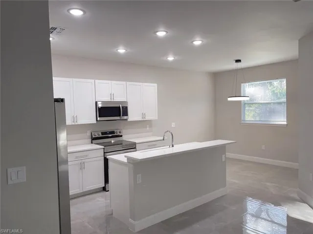 Kitchen with white cabinetry, light tile patterned floors, a kitchen island with sink, hanging light fixtures, and appliances with stainless steel finishes