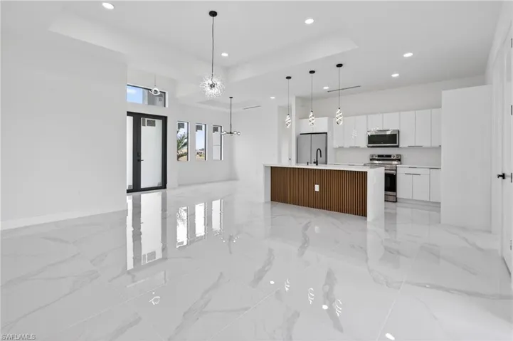 Open-concept living space featuring high ceilings, large format tile flooring, a contemporary kitchen island with slat wood paneling, white flat-panel cabinetry, and recessed lighting