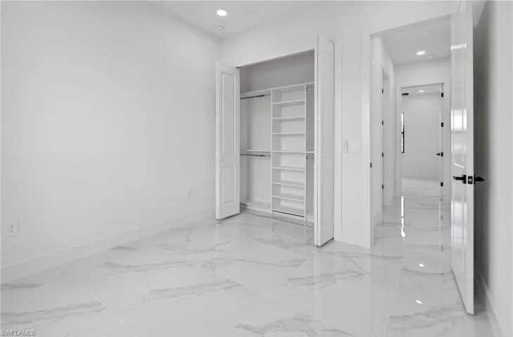 Interior room featuring large format tile flooring, a built-in closet with shelving and hanging rods, recessed ceiling lighting, and a white paneled door with black hardware