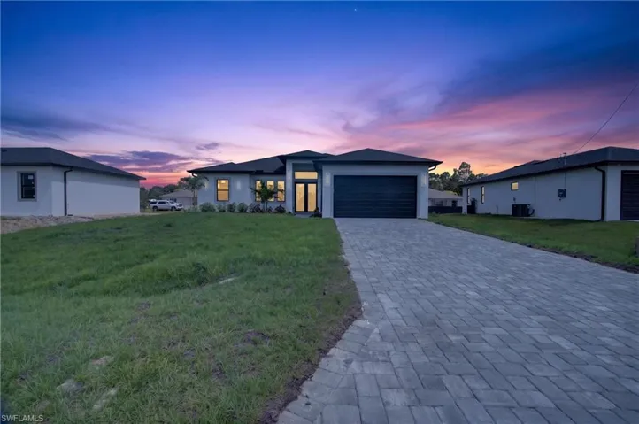 Contemporary home featuring a paver driveway, dark garage door, and light-toned exterior stucco