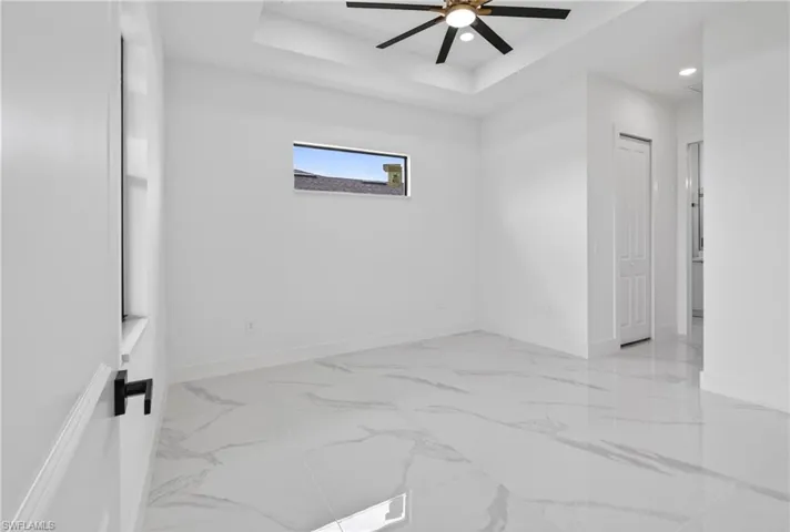 Spacious room featuring large format tile flooring, a tray ceiling, and a contemporary ceiling fan