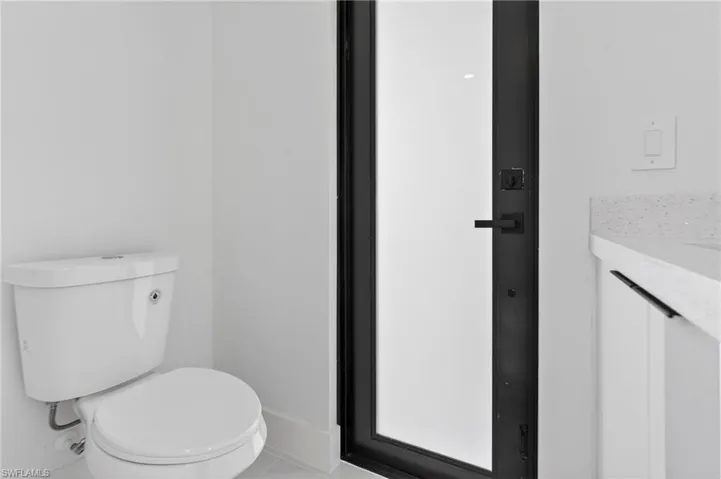 Contemporary bathroom featuring a white toilet, black-framed door with frosted glass, and a vanity with a light-colored countertop