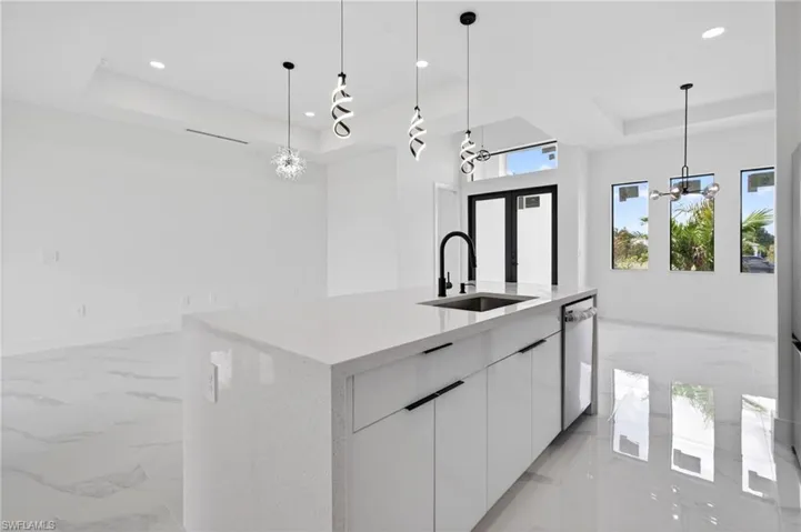 Open-concept space featuring a white quartz-finish island with an undermount sink and matte black faucet, modern white cabinetry with matte black hardware, and an integrated dishwasher
