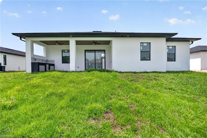 Rear exterior featuring a covered patio, outdoor kitchen, ceiling fans, and sliding glass doors
