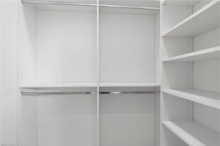 Custom closet system featuring white shelving, multiple hanging rods, and adjustable shelf heights