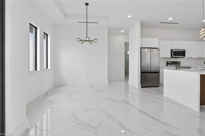 Open-concept living space featuring large format marble-look tile flooring, a contemporary linear chandelier, tray ceiling, and recessed lighting