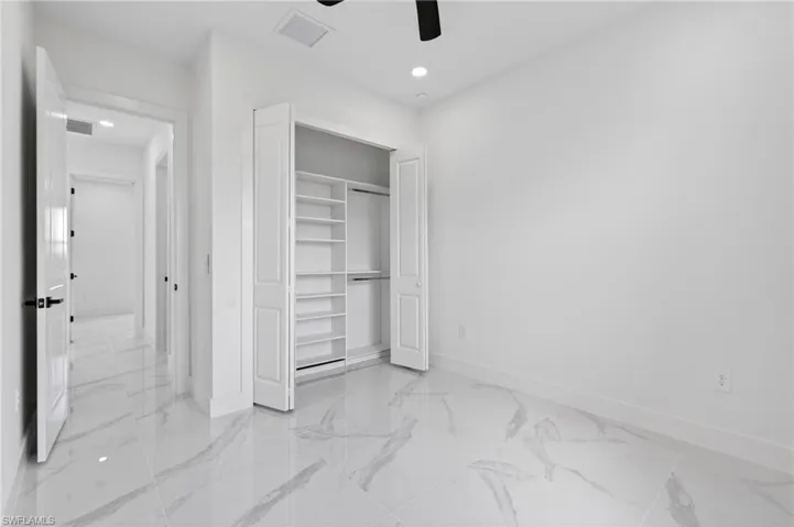 Interior room featuring large format marble-look tile flooring, white walls, and a built-in closet with shelving and hanging rods