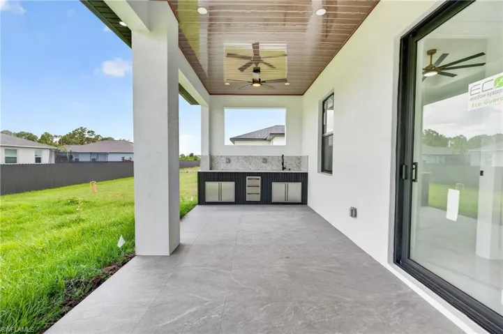 Covered patio with large format tile flooring, a built-in outdoor kitchen with a tile backsplash, and a wood-finish ceiling with integrated lighting and ceiling fans