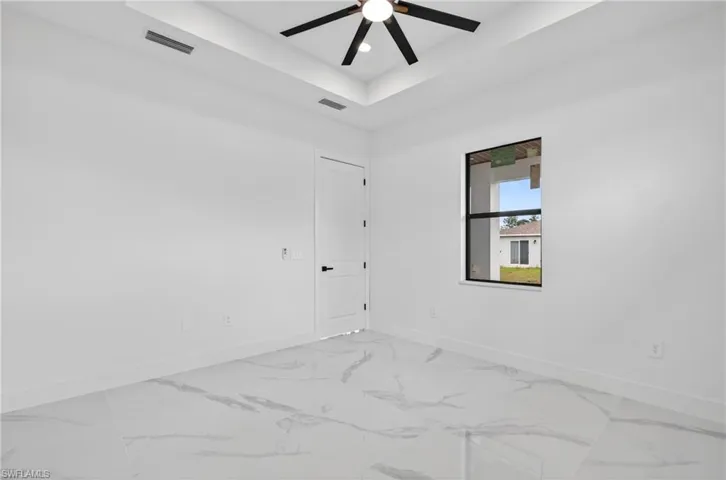 White-tiled flooring with gray veining, white walls, and a tray ceiling with a black ceiling fan