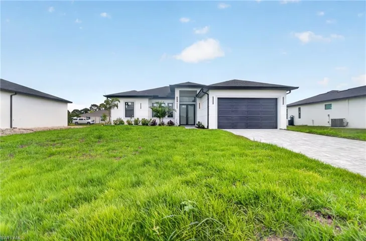 Contemporary white stucco exterior with a dark grey garage door, black-framed windows, and an extended paver driveway