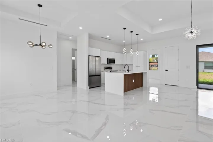 Open-concept living space featuring high-gloss marble-look flooring, a modern kitchen with a wood-finish island, stainless steel appliances, and contemporary lighting fixtures