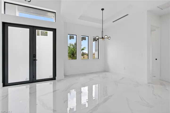 Contemporary entry space featuring double doors with transom window, three vertical windows, a modern multi-bulb chandelier, and white marble-look flooring