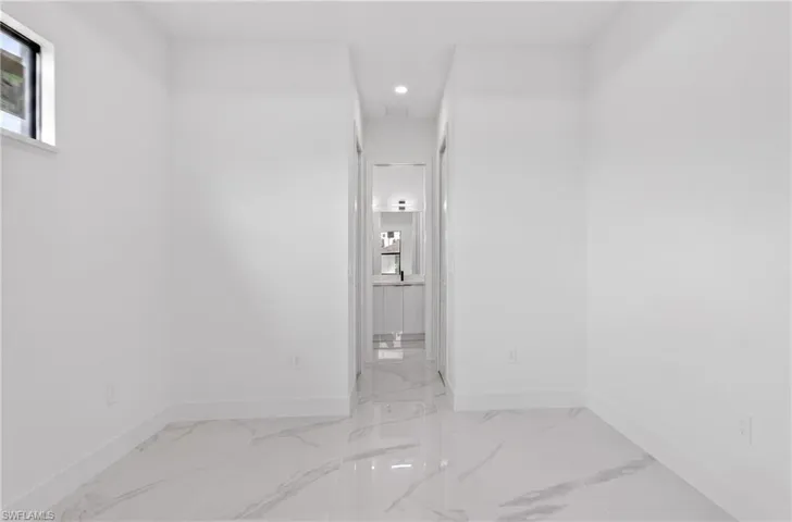 Spacious interior room with white walls, baseboards, and large format marble-look tile flooring