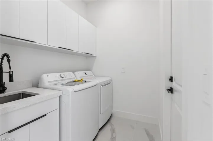 Contemporary laundry space featuring white cabinetry, a light-toned countertop, and a stainless steel sink with a matte black faucet